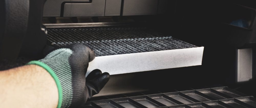 Mechanic hand installing car air conditioner filter into the air filter slot in the back of the document storage compartment in the car